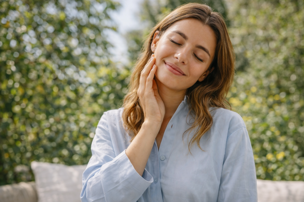Woman with glowing healthy skin gently touching her face in soft natural light with a clean blurred background